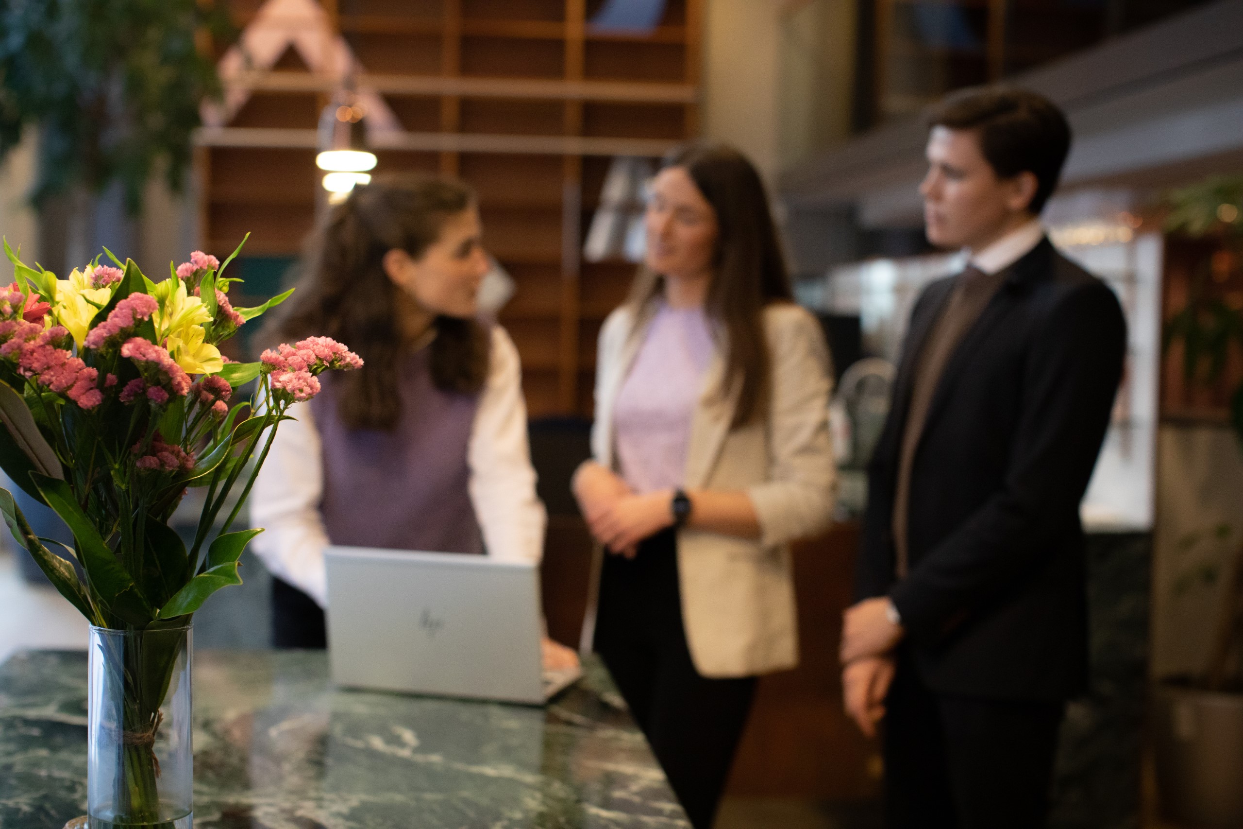 Faded out working people standing and discussing behind tabletop with flowers.